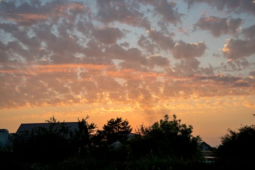 over the roofs of houses beautiful sunset . as if drawn by an artist's brush , poured by different colors. Clouds radiate warmth and a feeling of complete harmony. this sunset