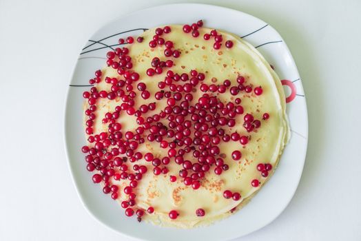 Pancakes with red currant berries in the plate on a white background