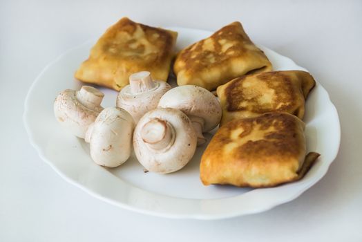 Fried pancakes with fillings and mushrooms in the white plate on a white background