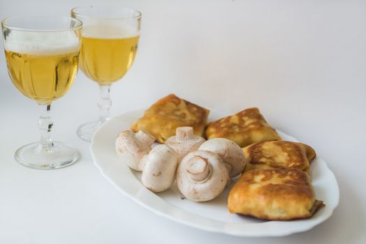 Fried pancakes with fillings, mushrooms and glass of beer in the white plate on a white background