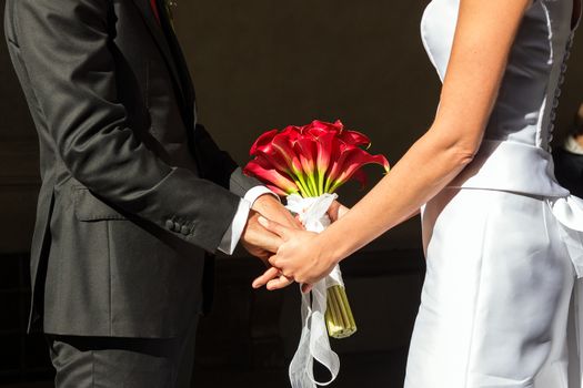 the hands of the newlyweds are intertwined touch of a bouquet of red flowers
