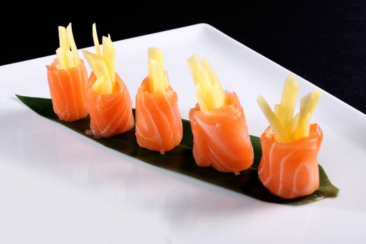 rolls of salmon on white plate, black background