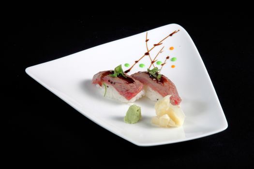 portion of sushi with vegetables on white plate, black background