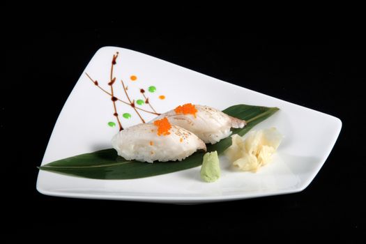 portion of sushi with vegetables on white plate, black background