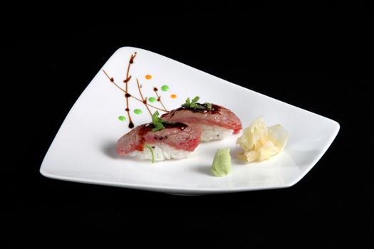 portion of sushi with vegetables on white plate, black background