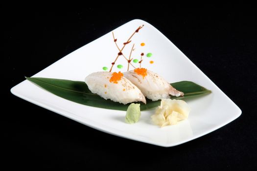 portion of sushi with vegetables on white plate, black background