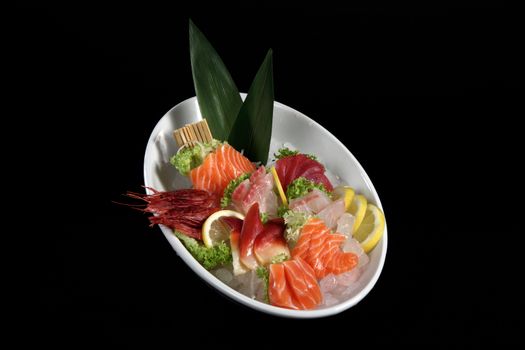 round plate of sushi and sashimi on black background