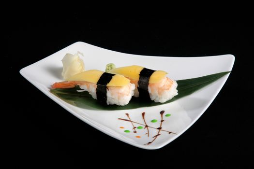 portion of sushi with vegetables on white plate, black background