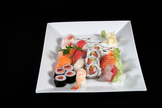 various sushi and sashimi with wasabi on white plate, black background