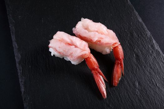 two sushi shrimp on slate plate, black background