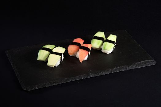Vegetable sushi on flat slate, black background
