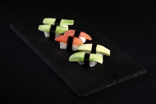 Vegetable sushi on flat slate, black background