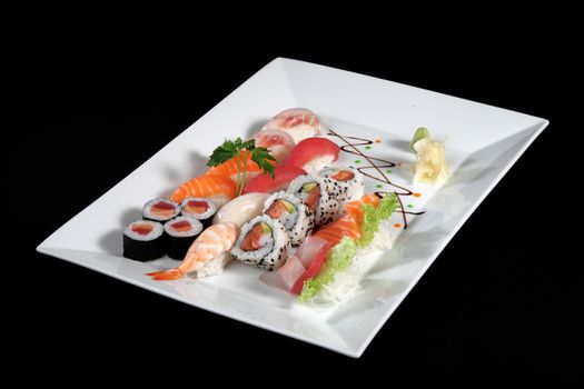 various sushi and sashimi with wasabi on white plate, black background