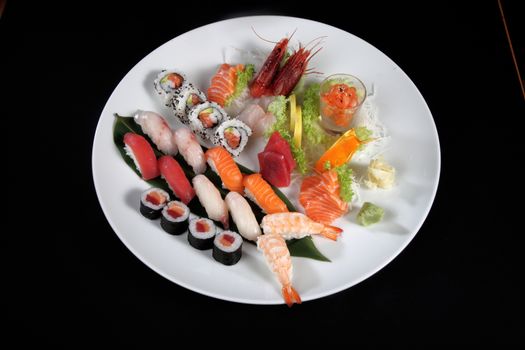 round plate of sushi and sashimi on black background