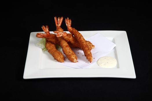 breaded prawns with vegetables and sauce in white plate on a black background