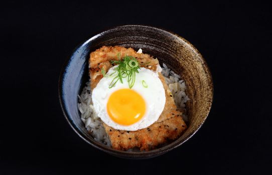 bowl with fried fish, rice and egg on a black background