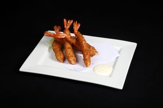 breaded prawns with vegetables and sauce in white plate on a black background