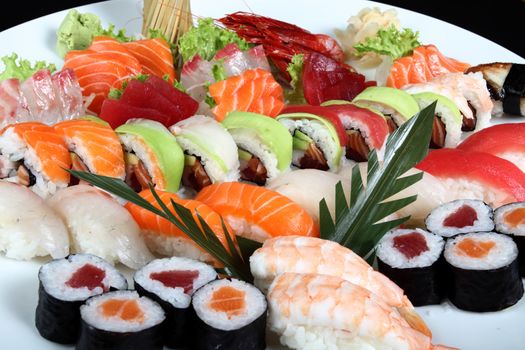 close-up sushi and sashimi mixed on round white plate on a black background