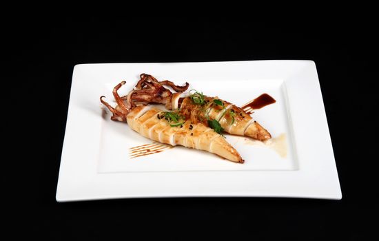 grilled squid with decoration of vegetables in white plate on a black background