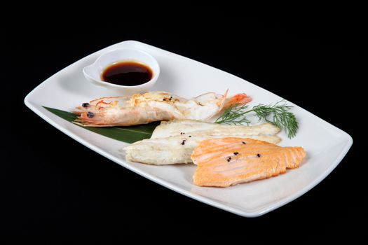 mixed fish grilled with sauce in white plate on a black background