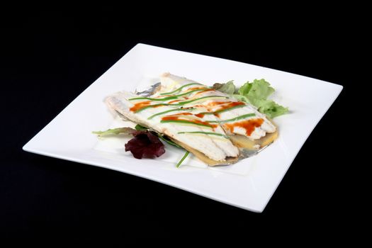 sea bass with vegetables in a square dish on a black background