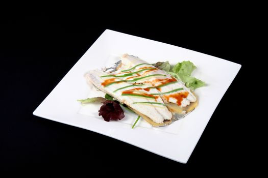 sea bass with vegetables in a square dish on a black background