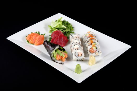 sushi and sashimi with wasabi and vegetable in white plate on a black background