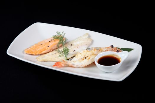 mixed fish grilled with sauce in white plate on a black background