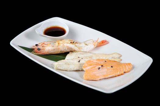 mixed fish grilled with sauce in white plate on a black background