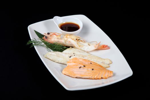 mixed fish grilled with sauce in white plate on a black background