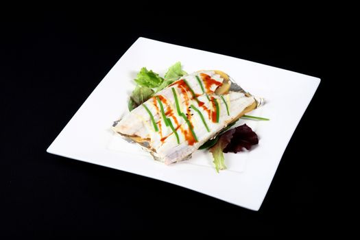 sea bass with vegetables in a square dish on a black background