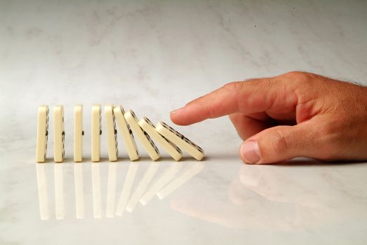 row of dominoes pushed by hand, on neutral background