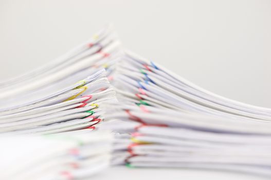 Pile overload paper of receipt and report with colorful paperclip have blur pile document foreground and background on white table.