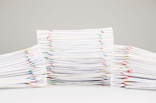 Pile overload paperwork of receipt and report with colorful paperclip have dual blur pile document foreground on white table.