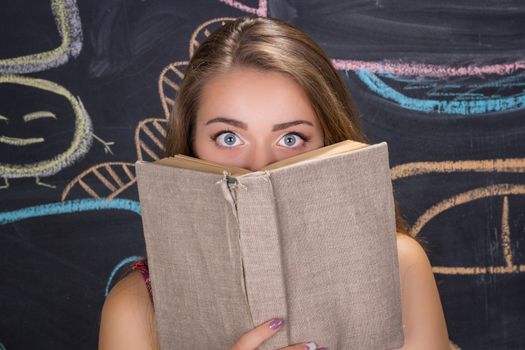Perplexed  young student girl in red dress and red glasses reading a book hides behind it
