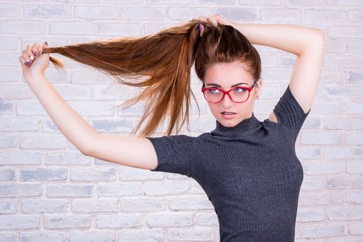 Young beautiful girl model with long hair in grey dress pulls her hair tail