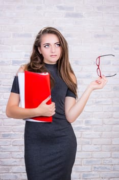 Young beautiful girl model with long hair imitates business lady, office manager or administrator with red folder of documents