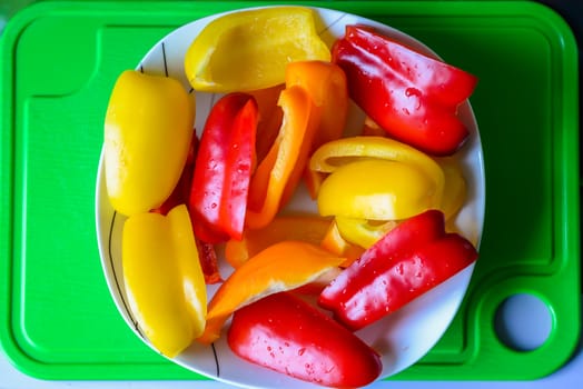 Slices of bell peppers in a white plate on the green plastic board