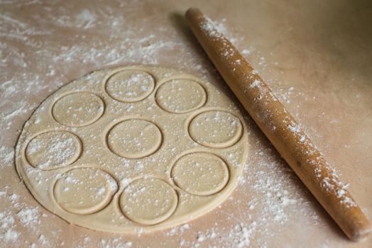 The dough rolled with circles and rolling pin for made ravioli on a wooden table