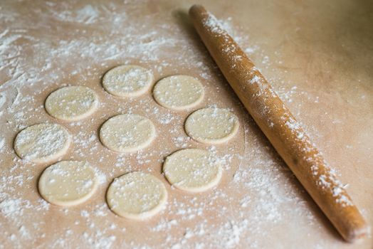 The dough rolled with circles and rolling pin for made ravioli on a wooden table