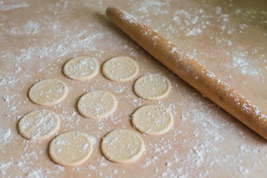 The dough rolled with circles and rolling pin for made ravioli on a wooden table