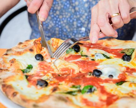 Close-up of woman hands cutting pizza outside at restaurant, selective focus.