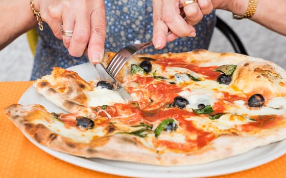 Close-up of woman hands cutting pizza outside at restaurant, selective focus.