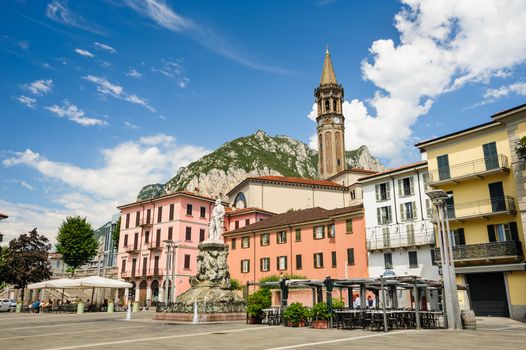 Lecco, Italy - August 17th, 2016: Central streets of Lecco town, with cafe and bell tower. Monument of Mario Cermenati at foreground