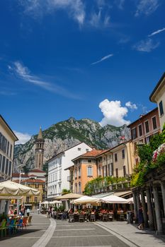 Lecco, Italy - August 17th, 2016: Central streets of Lecco town, with people relaxing in outdoor cafe and bell tower.