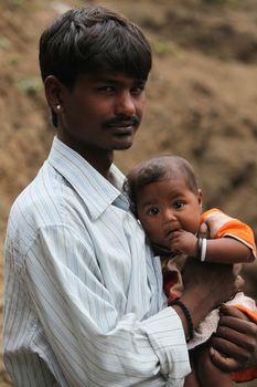 A portrait of a  poor Indian worker holding his baby in his arms
