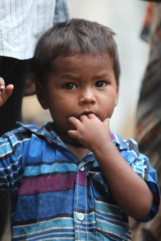 A portrait of a poor little Indian boy putting finger in his mouth.