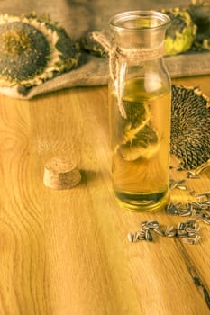 Bottle with cold pressed oil on a wooden table with sunflower plants and seeds all over it