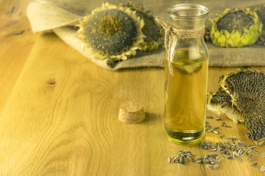 Sunflower oil in a glass bottle on a wooden table and sunflower plants in the background