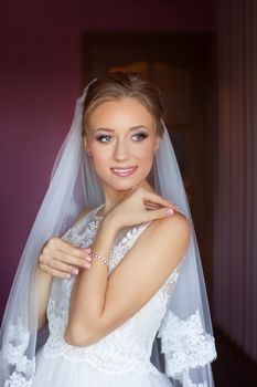 Portrait of beautiful bride with fashion veil posing on bed at wedding morning. Makeup. Brunette girl with long wavy hair styling. Wedding dress.